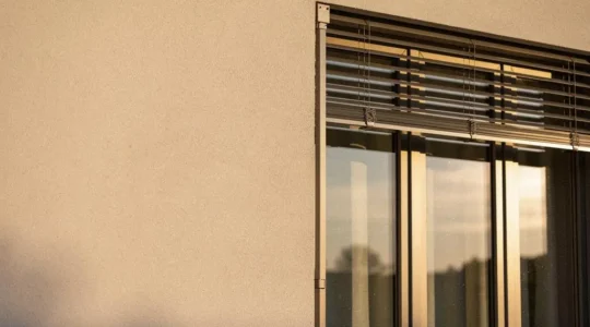 Façade d'une maison française contemporaine avec de larges fenêtres aluminium et une protection solaire extérieure, illustrant la performance et la durabilité des menuiseries