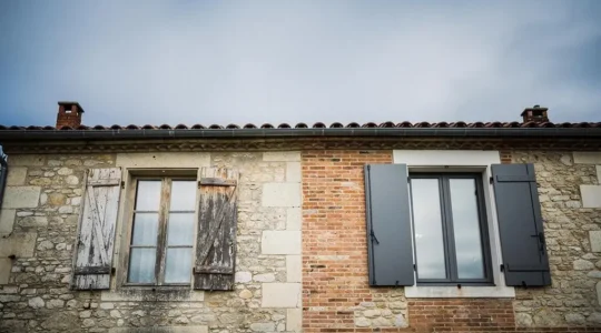Facade d'une maison de caractere francaise dont les menuiseries neuves contrastent avec la pierre ancienne, illustrant la transformation esthetique
