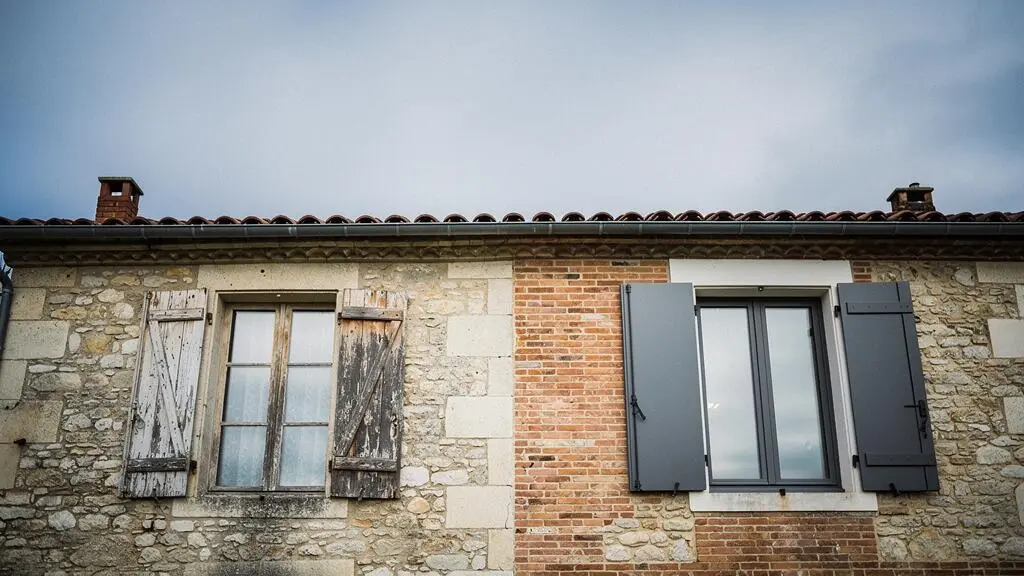 Facade d'une maison de caractere francaise dont les menuiseries neuves contrastent avec la pierre ancienne, illustrant la transformation esthetique