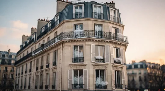 Facade d'un immeuble haussmannien parisien au petit matin, avec de grandes fenêtres anciennes laissant deviner une legere condensation, symbole des pertes de chaleur liees aux menuiseries defaillantes