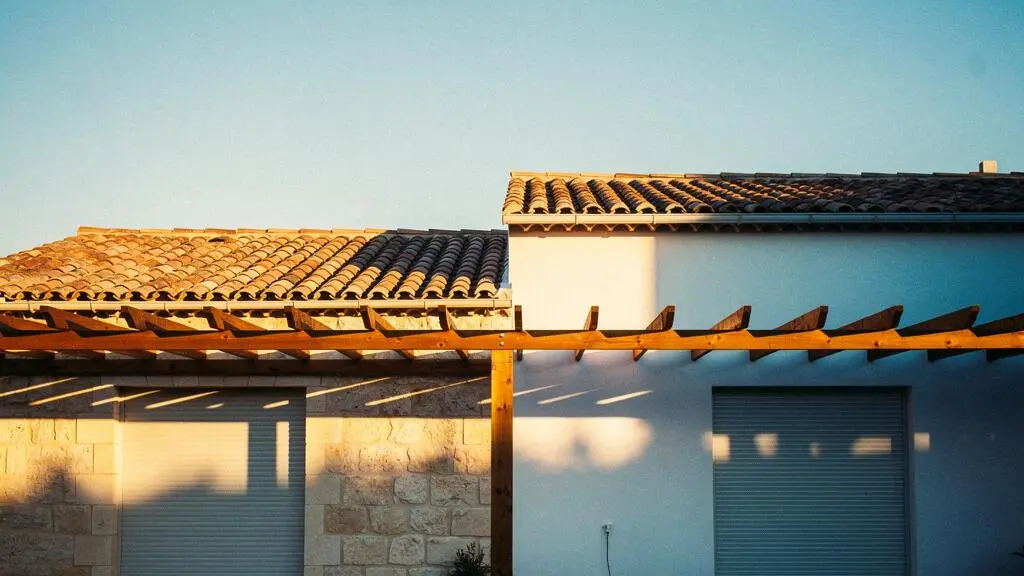Maison contemporaine française protégée du soleil par des volets et une pergola, illustrant le rafraîchissement naturel sans climatisation