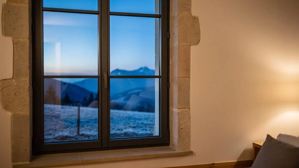 Fenêtre à triple vitrage d'une maison française vue de l'intérieur, contraste entre chaleur intérieure et paysage hivernal extérieur