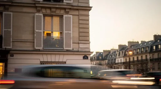 Fenêtre d'un appartement parisien avec store et volet fermés face à une rue animée, symbole de protection contre le bruit urbain